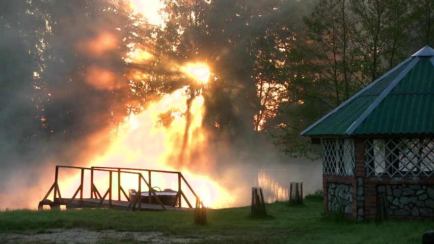 Sunrise through the trees on a background of lake. Above water the fog. The rays of the sun through the haze. Early morning beautiful sunrise on the lake