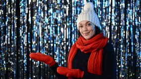 Beautiful Christmas winter woman in warm knit hat, muffler and gloves showing on the palm blank copy space over lights background, sliding video