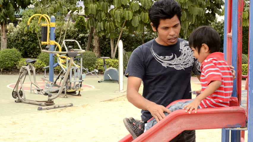 Asian father and son playing together on a slide in a park.