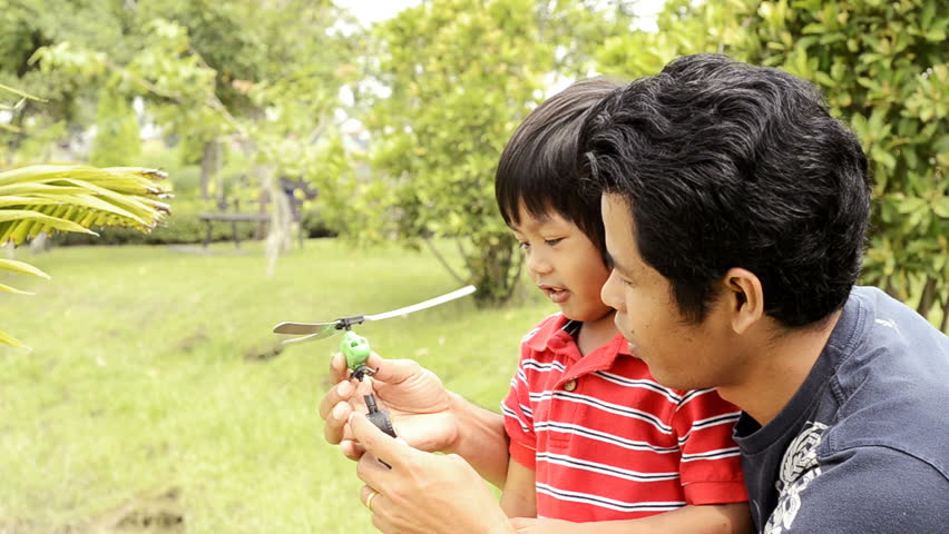Asian father and son playing together with a toy helicopter in a park.