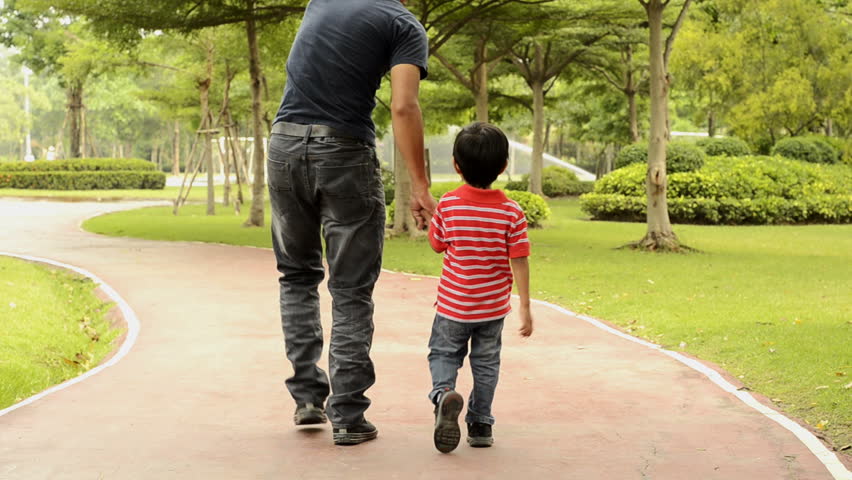 Asian father and son walking together in a park.