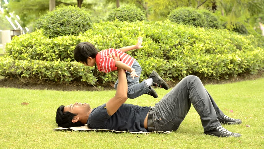 Asian father and son playing together on the grass in a park.