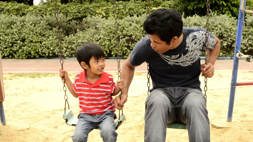 An Asian father and son playing together on a swing set.