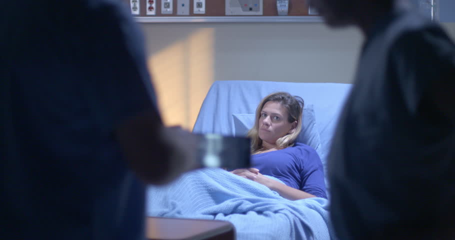 Young woman rests in hospital bed while medical staff look at X rays on tablet computer in foreground.  Focus on patient to start, with rack focus to X rays after.  Evening lighting. | Shutterstock HD Video #21174091