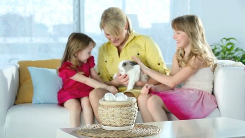Family spending time at home, mother holding an adorable bunny while daughters caressing it, Easter series