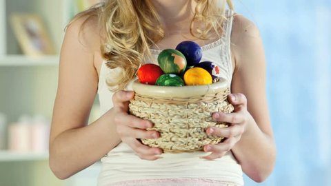 Pretty blond girl holding a basket full of colorful Easter eggs and smiling, camera moving bottom-upwards then down again Stock Video