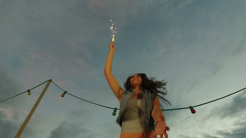 Low angle view of beautiful smiling woman holding firework candle and jumping on the rooftop terrace