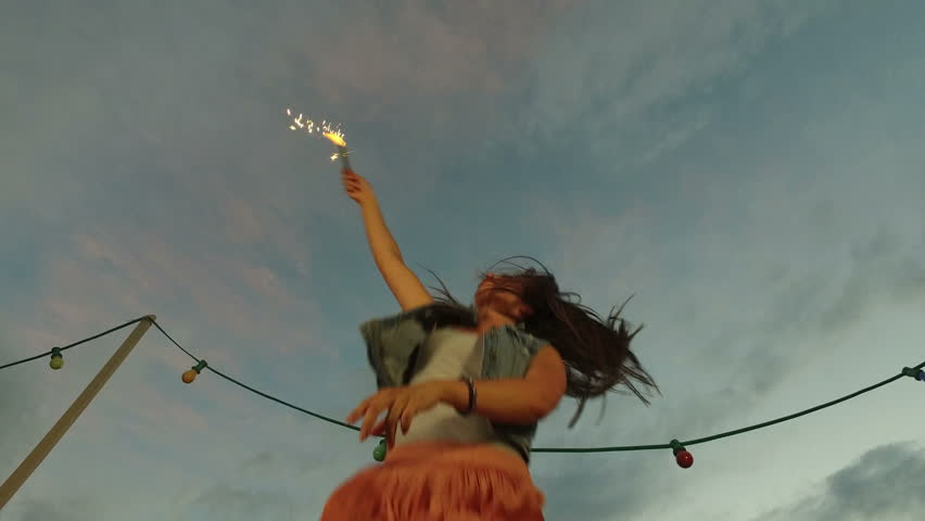 Low angle view of beautiful smiling woman jumping while holding firework candle on the rooftop terrace