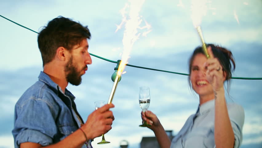Cute happy couple having fun dancing with firework candles in their hands at the rooftop terrace, graded