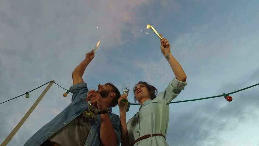 Under view of beautiful couple drinking champagne and waving with firework candles