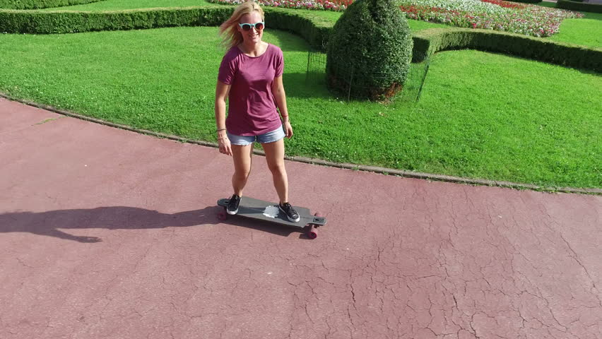Cheerful blonde woman riding on a longboard in the city park