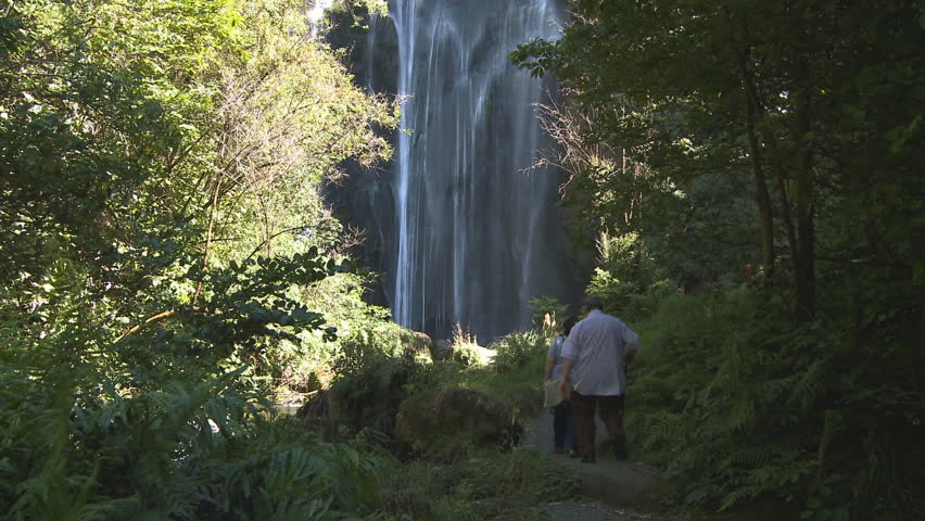A small group of people approach the base of a large waterfall in New Zealand