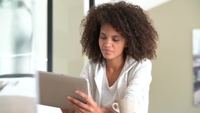 Mixed-race woman at home using tablet and drinking tea
