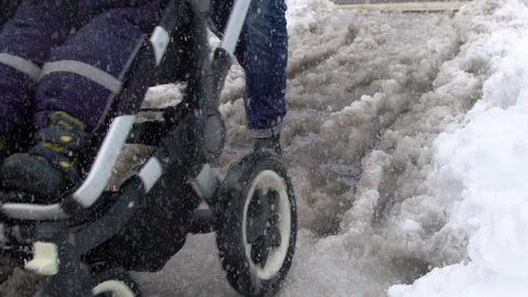 A dad pushing a stroller in slushy snow on a wintry day. Slow motion clip.