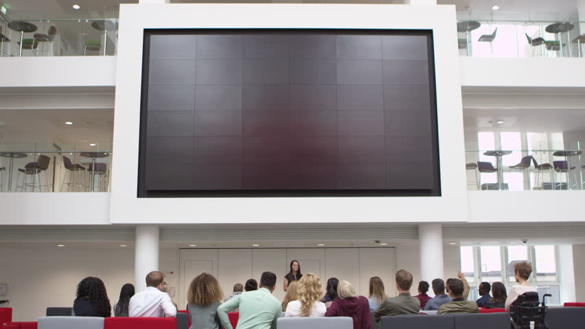 Students at a lecture watch a big screen in a university atrium, shot on R3D
