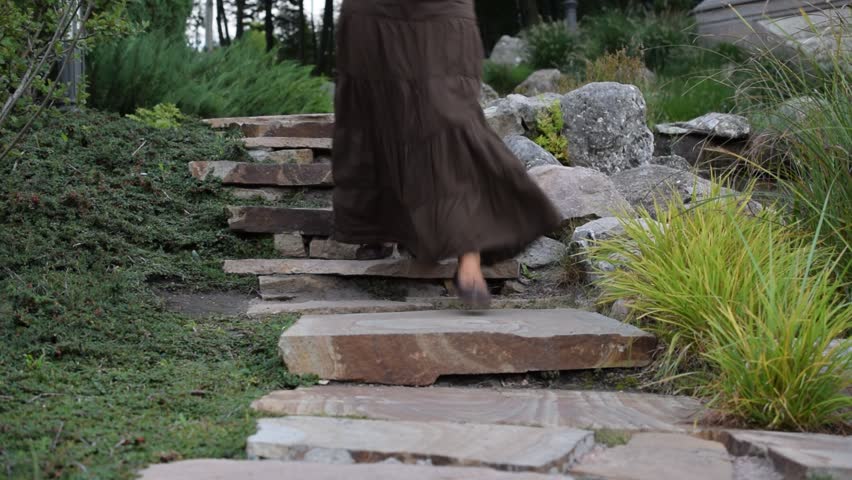 Feet of slim woman in mocassins and long brown skirt walking down stony stairs in park towards camera