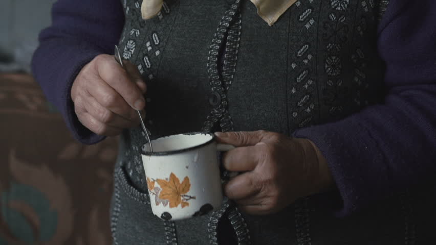 Old grandmother making food using metal mug