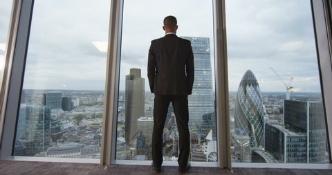 4K View from behind of young successful business executive looking out at view of the city. View from the window shows famous London skyline with iconic buildings. Slow motion.