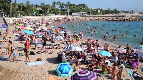 CANNES, FRANCE - JULY 27, 2016: Many people relax on the beach with colorful sun umbrellas. The city is one of the most popular and famous resorts of the Cote d azur