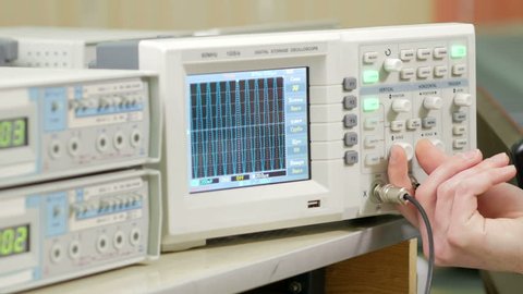 Men's engineering arm adjusts the oscilloscope for proper display of the electrical signal. Modern small industrial oscilloscope