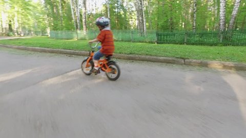 Little boy training to ride a bike and falls to the ground. Mom follows him.