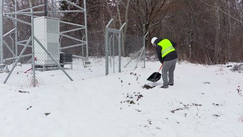 Worker with snow shovel working near fence