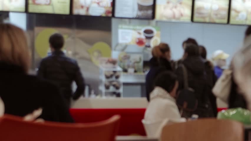Defocused people waiting fast-food in mall food court. Rear view, unrecognizable peple.