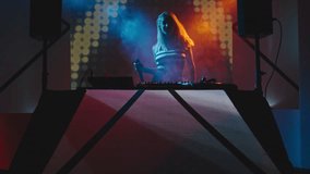 Female DJ with blond hair jumping and singing behind decks on concert in nightclub