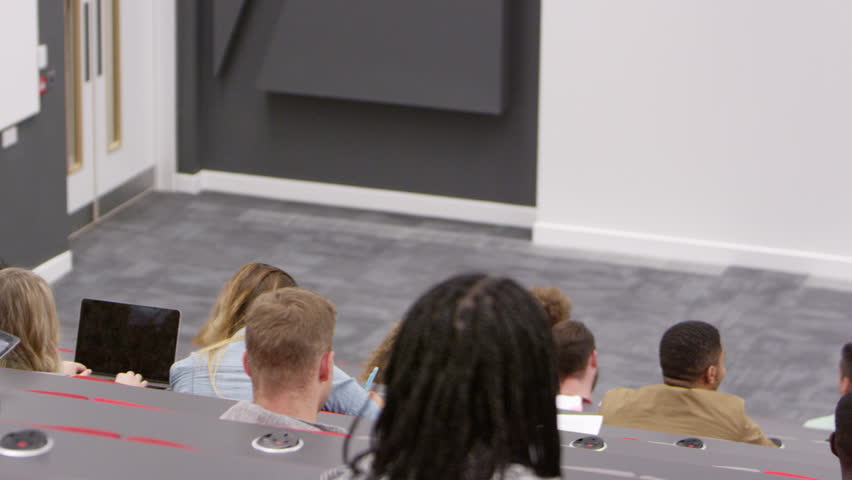 Teacher at lectern in lecture theatre, back row student POV, shot on R3D