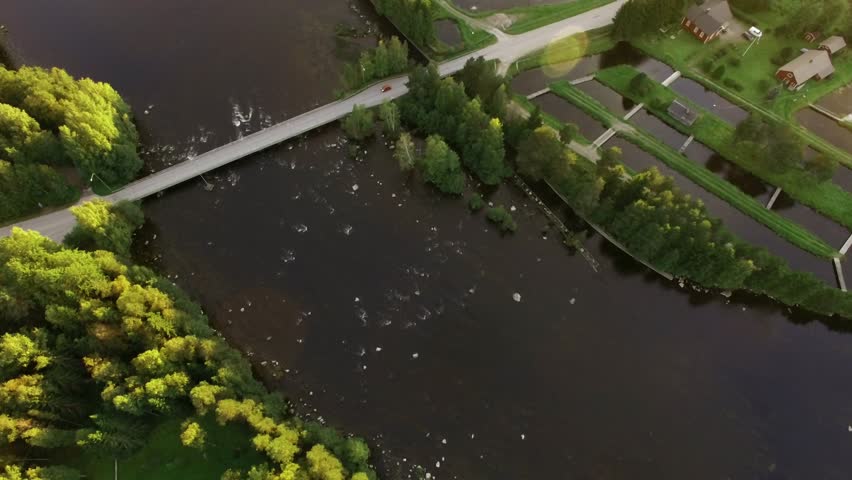 Fish farm pools in beautiful landscape by a streaming river in Finland, aerial tilt shot with lens flare of the evening sun.