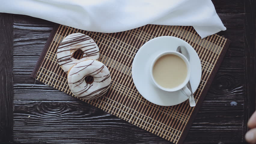 Man Stirs Sugar in a Cup of Coffee, Two Donuts on a Black Wooden Table, Top view