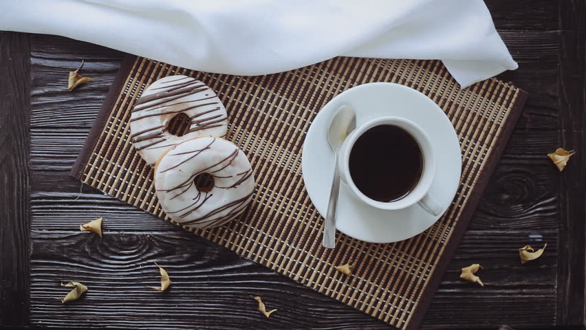 Man Pouring Milk into Coffee, Two Donuts and dry leaves decor on a Black Wooden Table, Top view