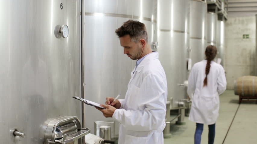 young man in coat taking notes in  fermenting section on wine factory