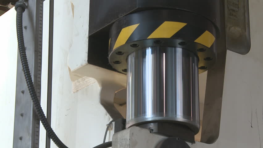 A large hydraulic ram on a metal press in a metal workshop