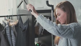 Attractive young woman shopping for clothes fashion designer browsing wardrobe. Clothing hanging on hangers at design studio. Small business owner. Showroom of designer clothes.