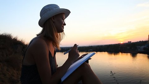 creative personality with a notebook on the riverside during sunset