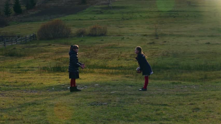 Two little beautiful girls playing with a ball on the nature at the sunset autumn