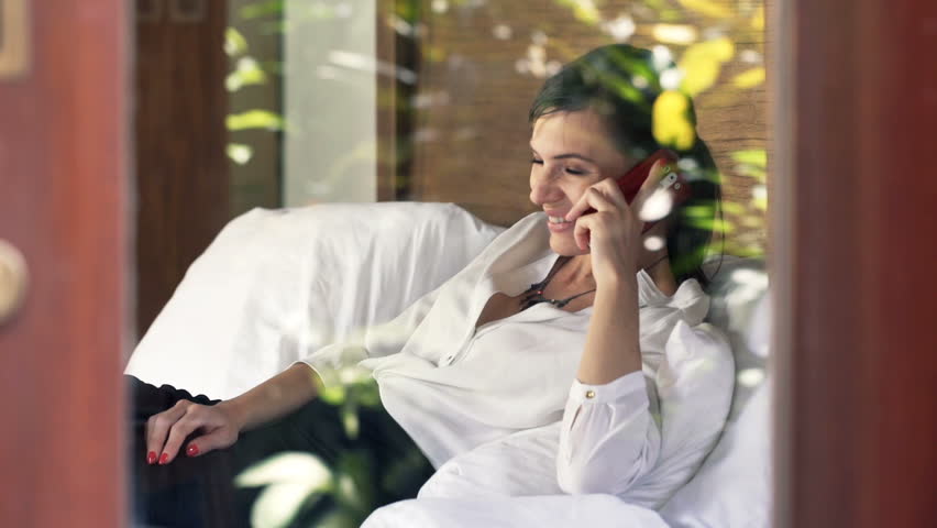 Young, pretty businesswoman talking on cellphone lying on bed at home
