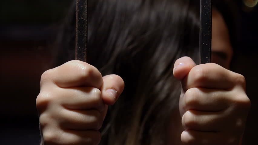 young woman grabs the bars of a prison with her hands