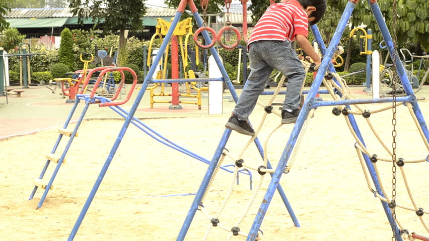 Young boy climbing down a rope ladder in a playground.
