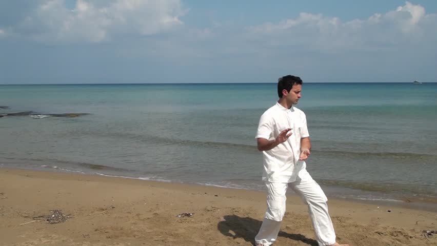 Handsome man practicing thai chi on the beach in the summertime