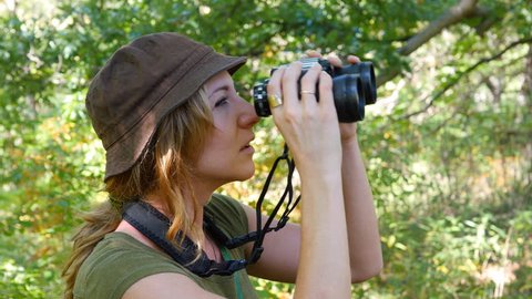 Female birdwatcher brings binoculars up to look at something.
