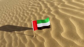 A small flag of United Arab Emirates flying on a sand dune in the desert.