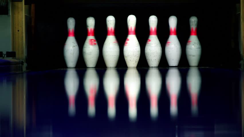 Ball rolls and beats skittles at bowling lane lit in dark, closeup view