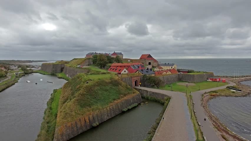 Drone flying towards ancient fortress with moat surrounded by water in cloudy sky