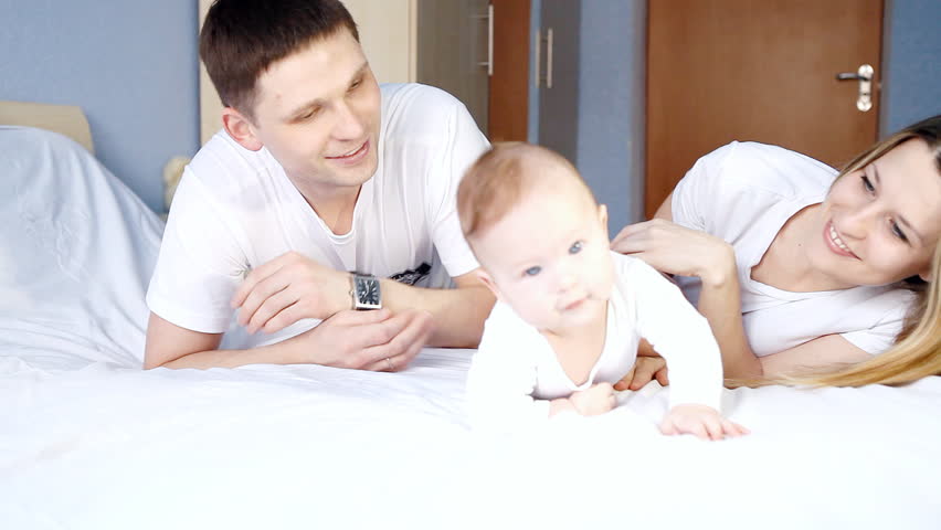 Happy family: father, mother and baby playing on the bed
