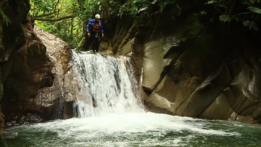 footage of a person crossing a waterfall on a zipline .locked down, wide angle