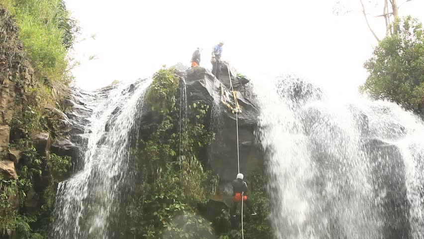 footage of a pesrson rappelling a waterfall.locked down, wide angle shot in