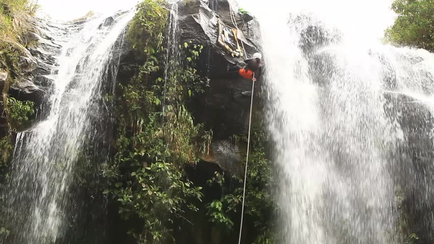 footage of a pesrson rappelling a waterfall.locked down, wide angle shot in