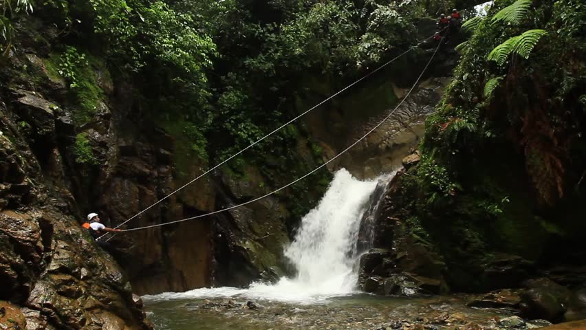 footage of a person crossing a waterfall on a zipline .locked down, wide angle